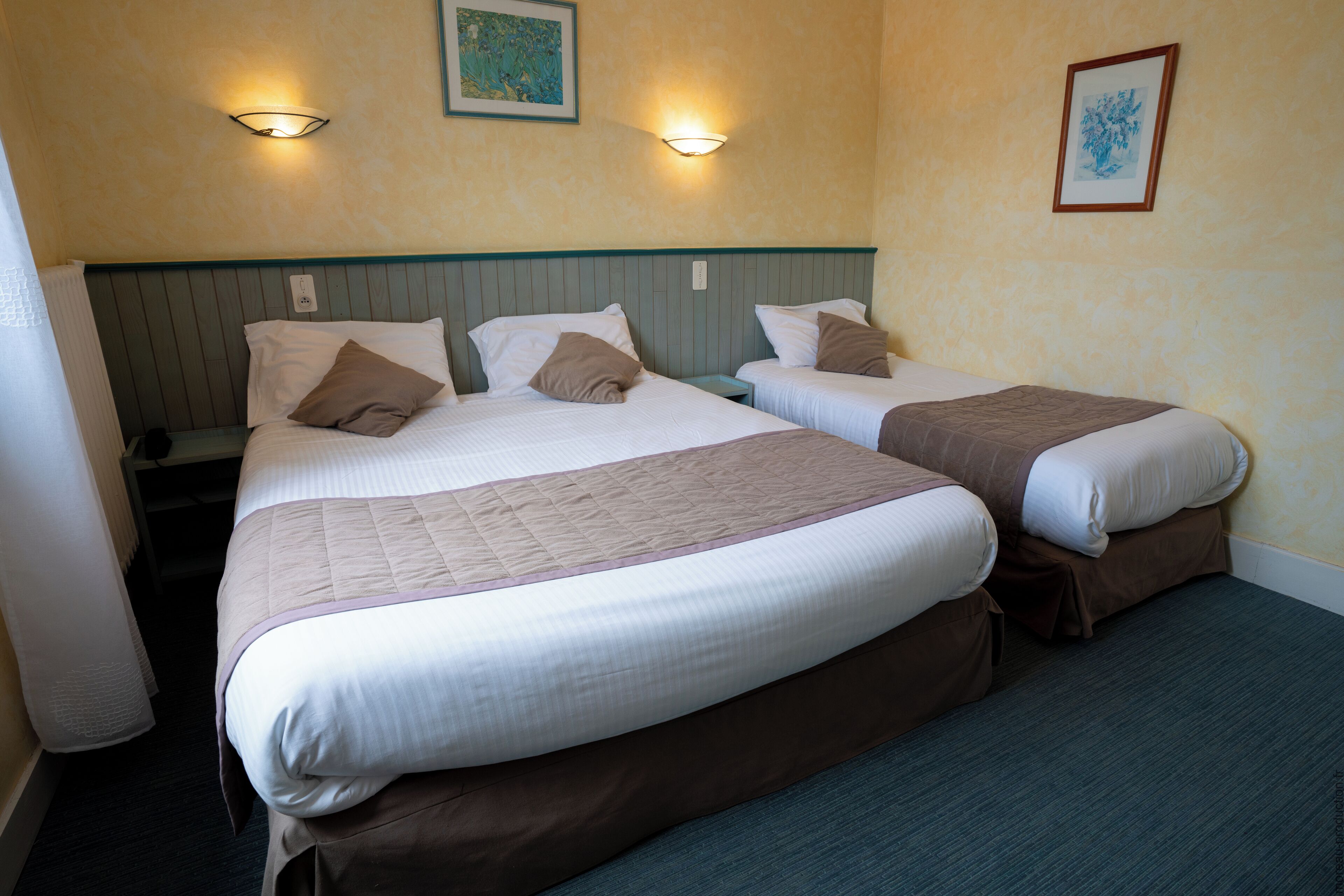 Une chambre d’hôtel avec deux lits simples, un grand lit et une table de chevet placée entre les deux.