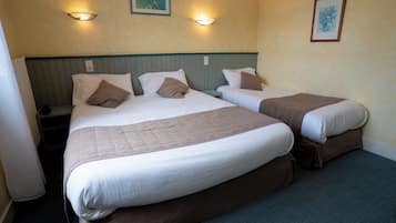 Une chambre d’hôtel avec deux lits simples, un grand lit et une table de chevet placée entre les deux.