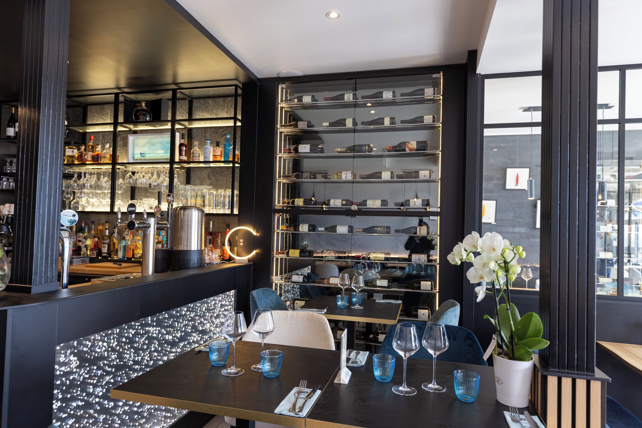 A modern bar area with shelves of liquor bottles, glasses, and a bar counter.