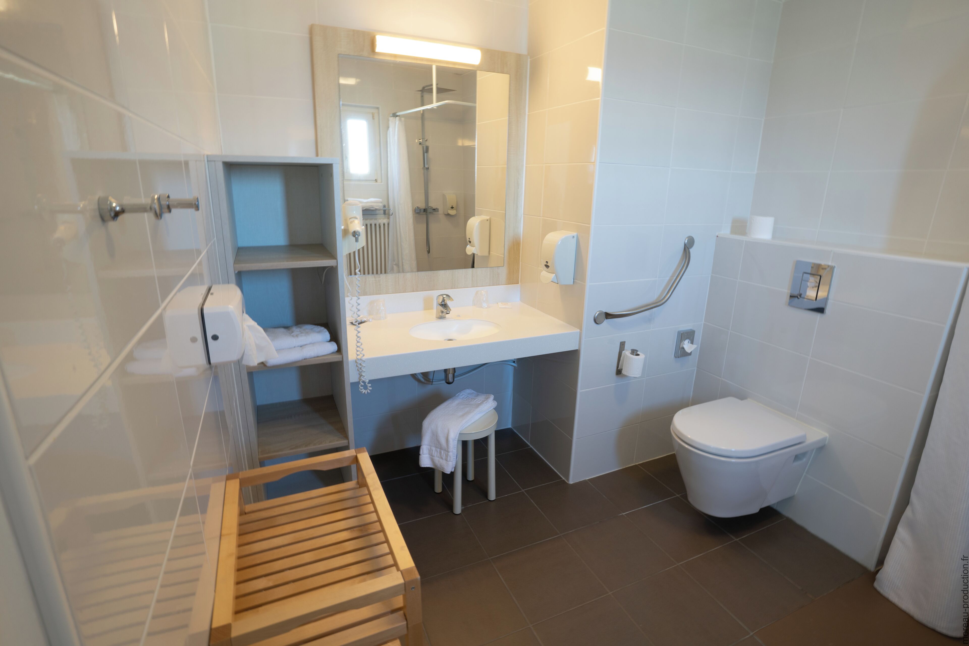 A modern bathroom with a shower, toilet, sink, and handrail.