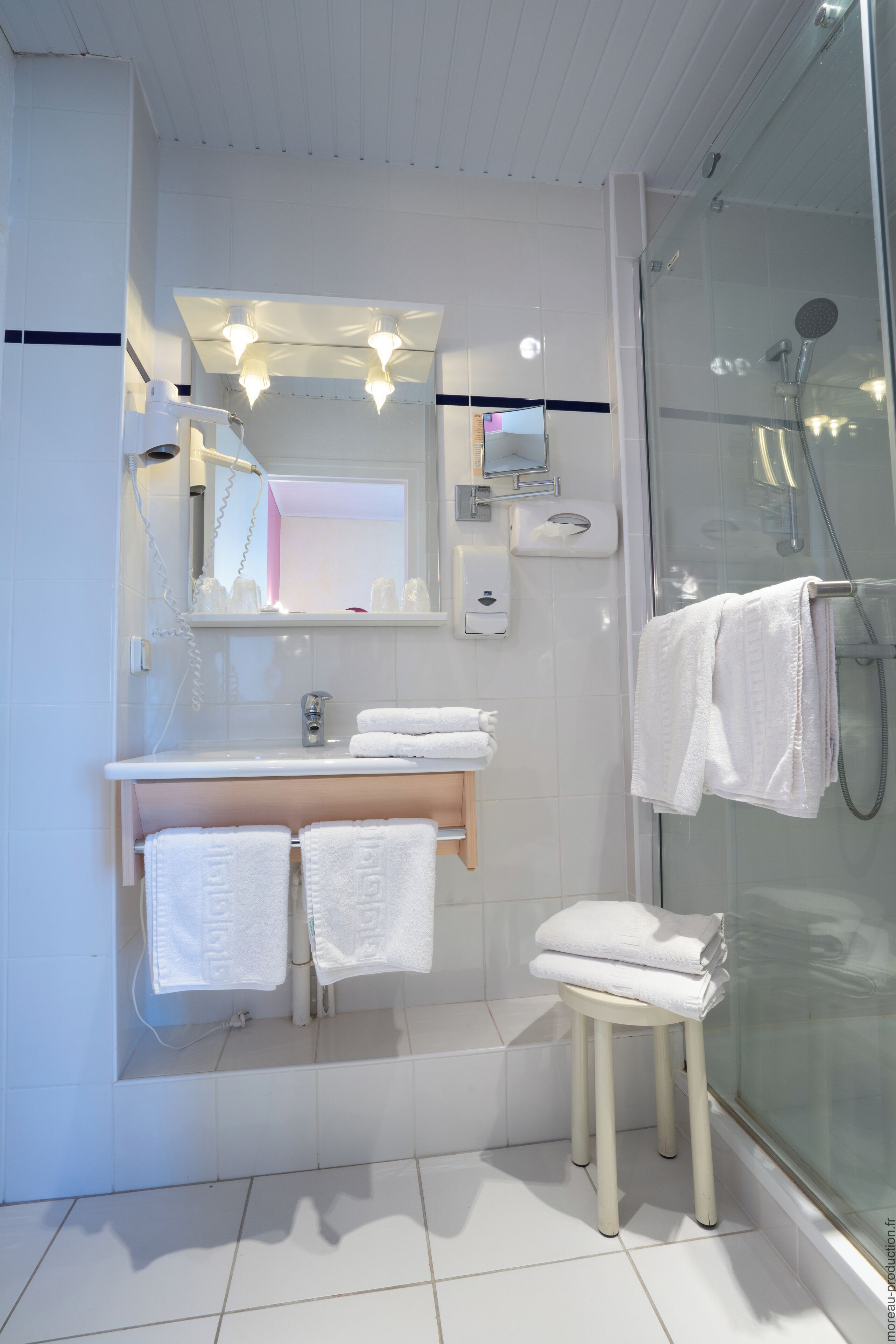 A modern bathroom with a glass shower enclosure, a vanity with a mirror, and a stool with towels.
