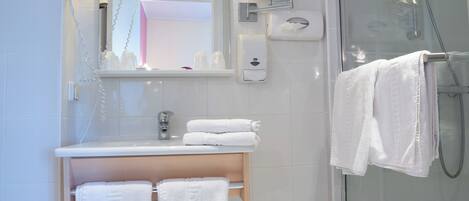 A modern bathroom with a glass shower enclosure, a vanity with a mirror, and a stool with towels.