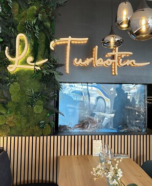 A restaurant interior with a sign reading "Le Turkoftin," a wooden wall with greenery, and a large aquarium with fish and a crab. - Hotel de la Mer (Quiberon)