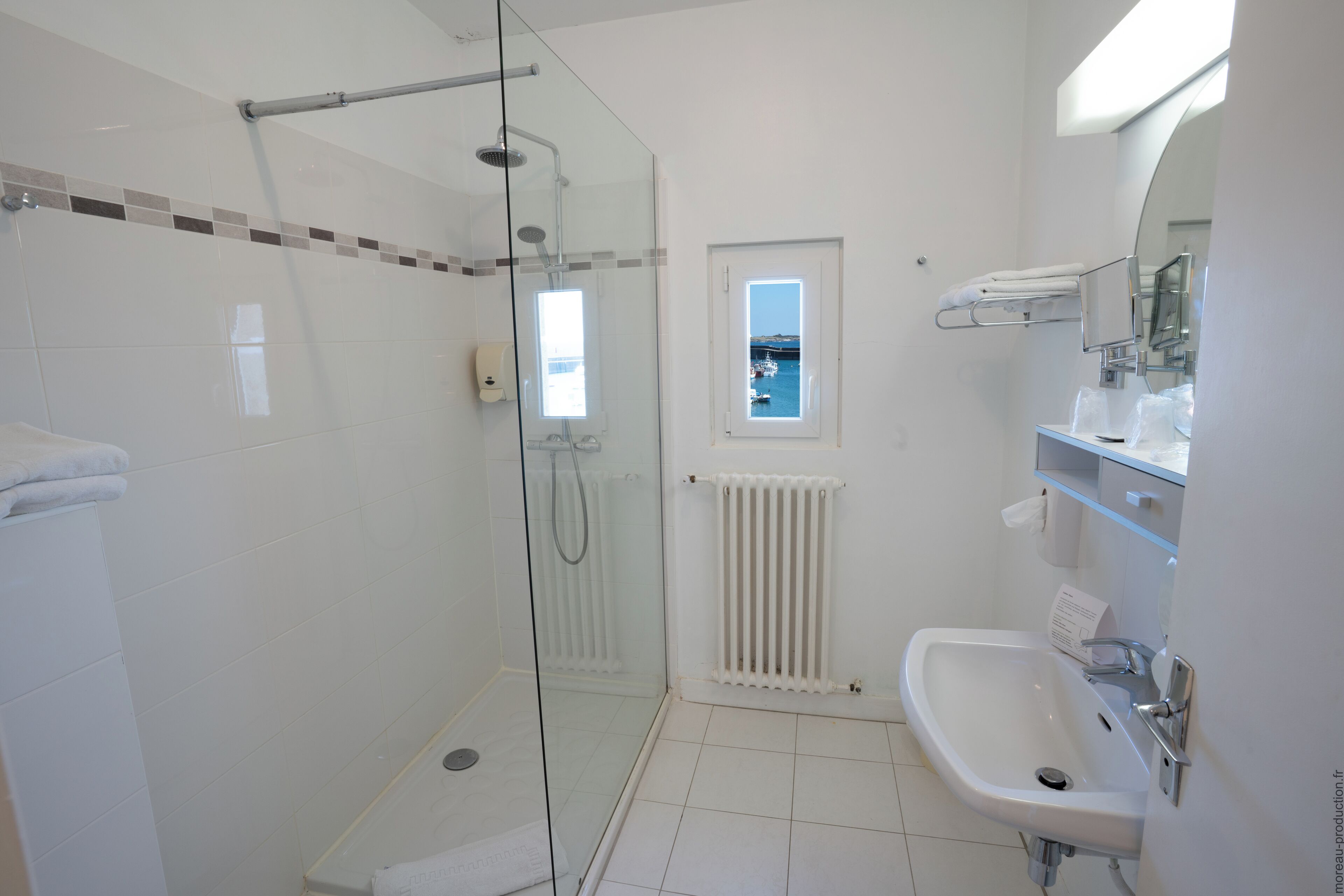 Un baño moderno con cabina de ducha de vidrio, un lavamanos blanco y una ventana con vista a barcos.