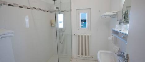 Un baño moderno con cabina de ducha de vidrio, un lavamanos blanco y una ventana con vista a barcos.