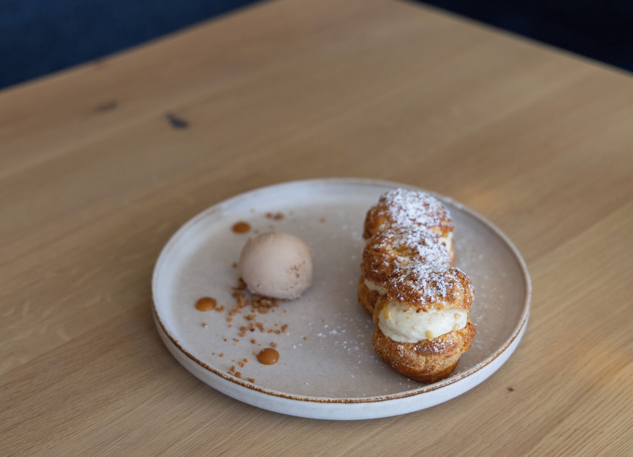 A dessert on a plate with a round edge, featuring a pastry with a creamy topping and a scoop of ice cream.