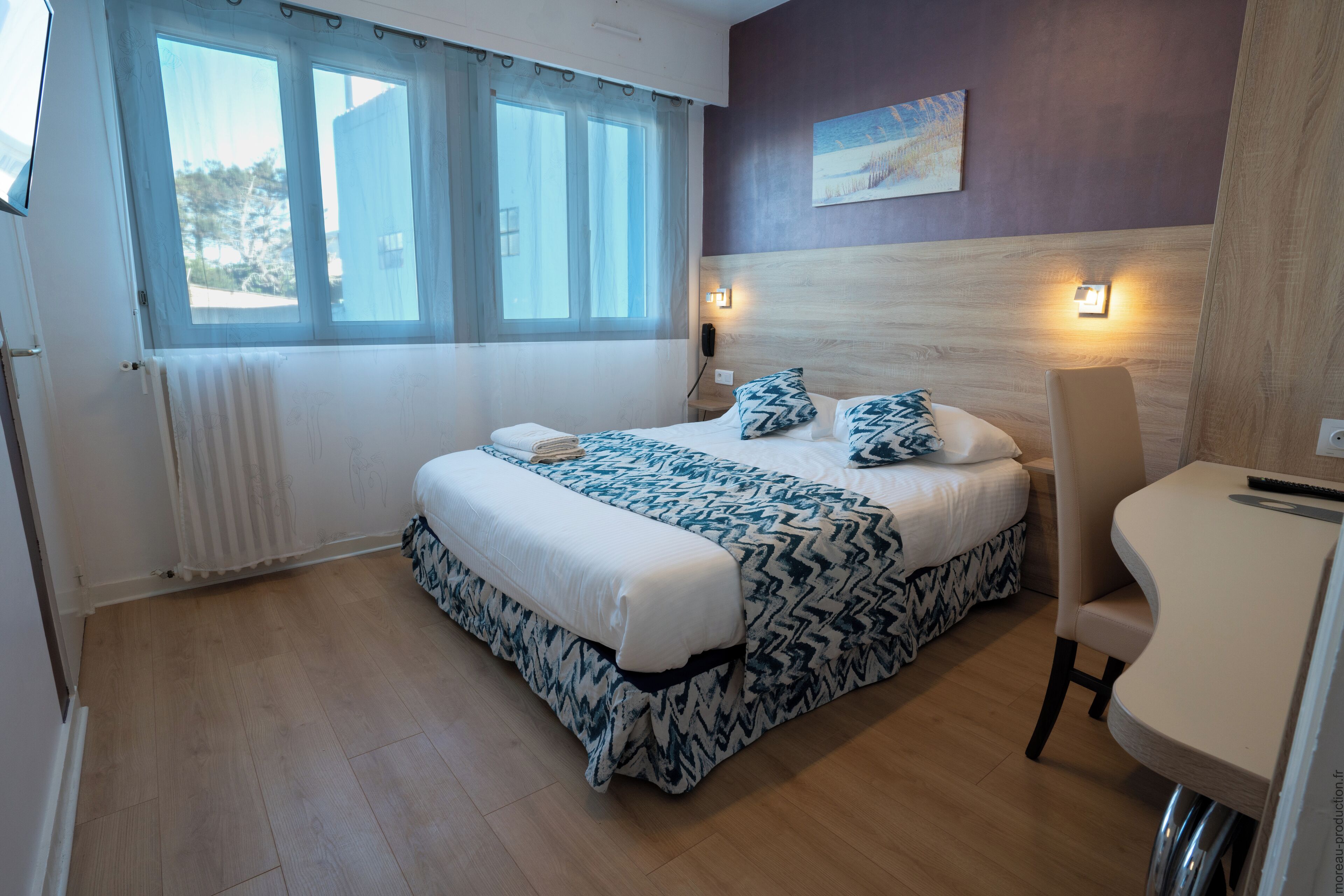 A bedroom with a bed, bedside table, chair, and a window with curtains.