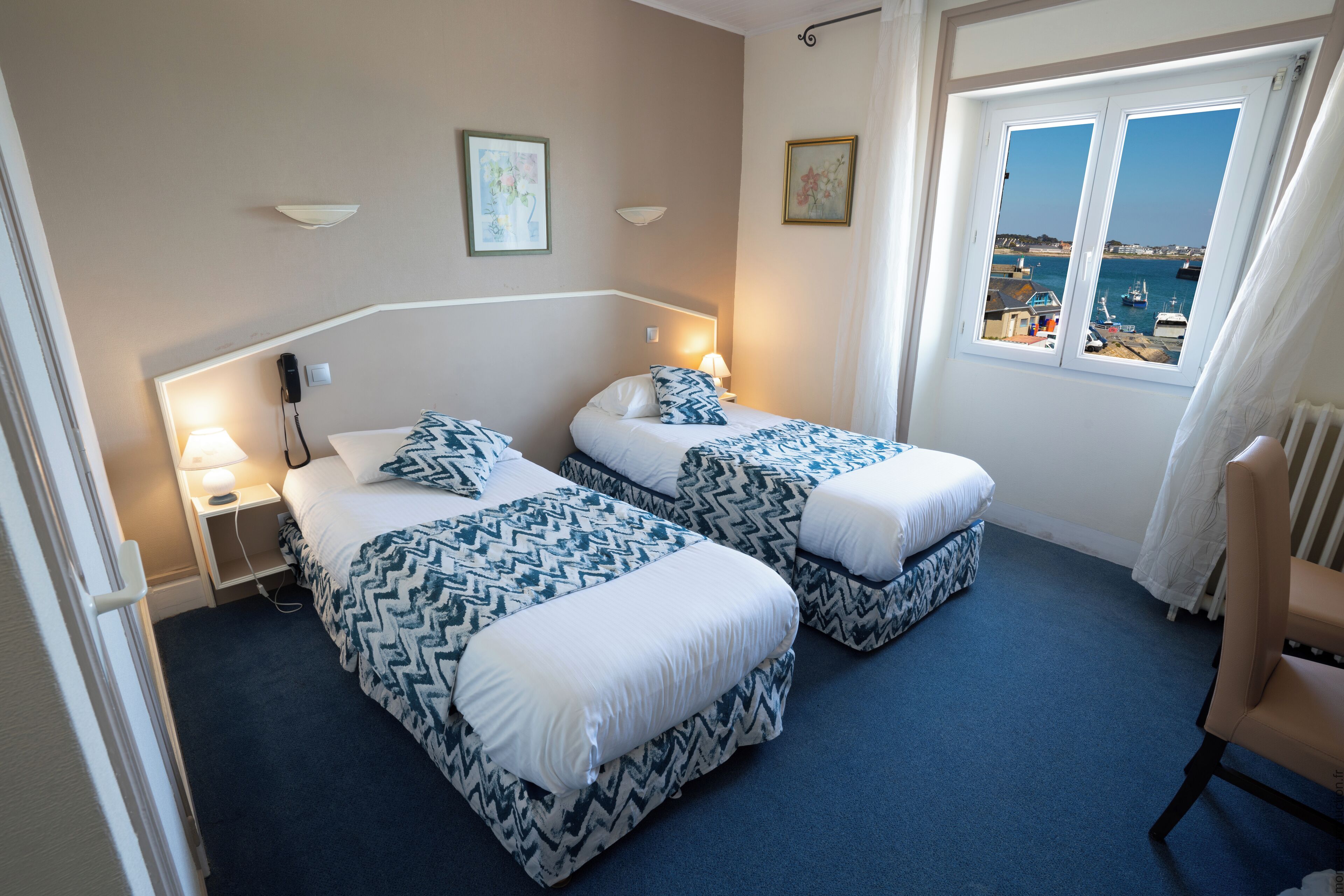 Una camera d'albergo con due letti, vista mare e una sedia.