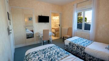A hotel room with two beds, a desk, a chair, a television, and a bathroom visible through an open door.