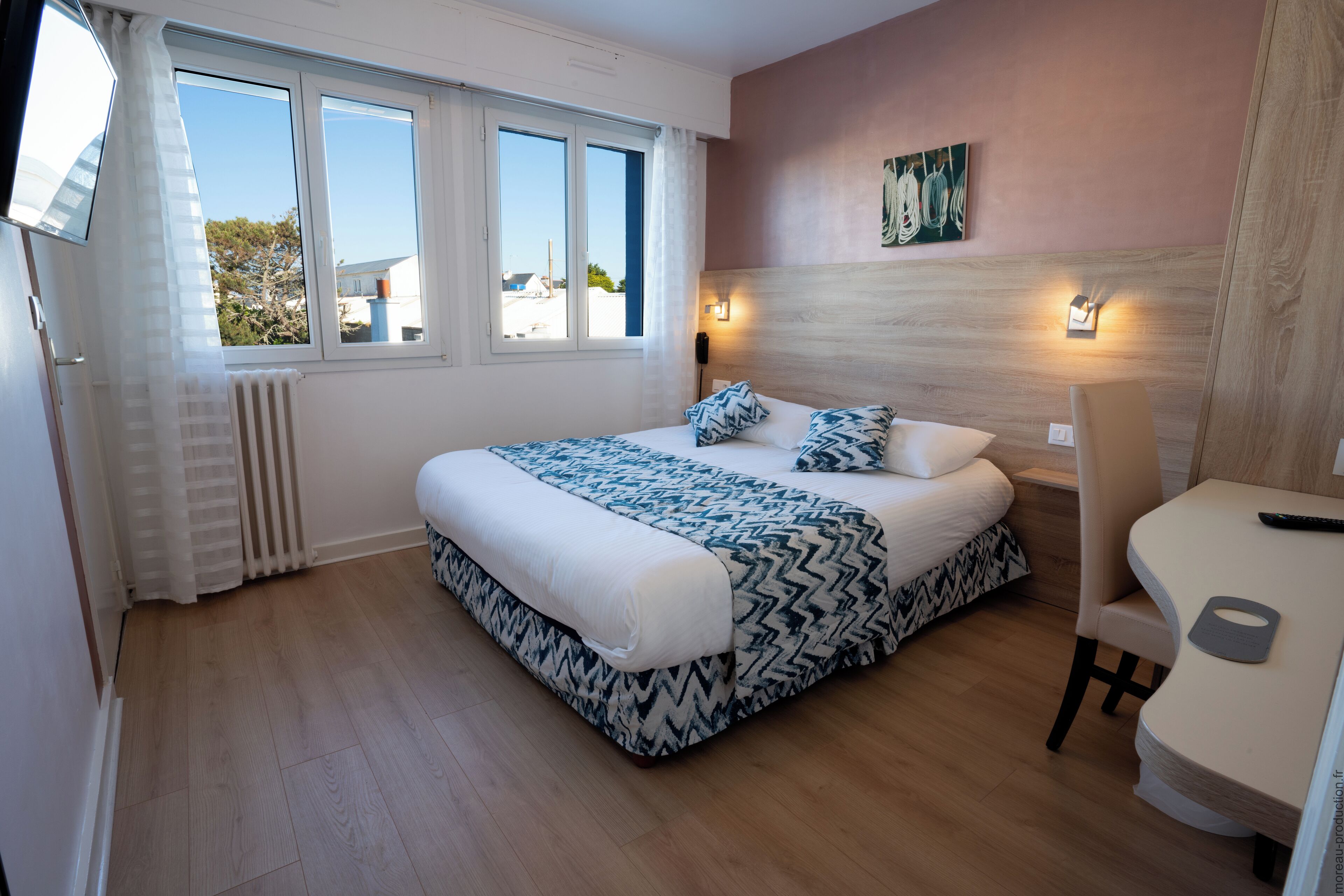 Ein Schlafzimmer mit einem großen Bett, einem Nachttisch, einem Sessel und Blick ins Freie.