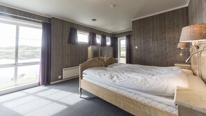 A bedroom with a large bed, wooden walls, a window with curtains, and a bedside lamp. - Bergsjøstølen (Al)