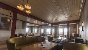 A spacious lounge area with wooden tables and green upholstered seating, featuring large windows and a high ceiling with exposed beams. - Bergsjøstølen (Al)