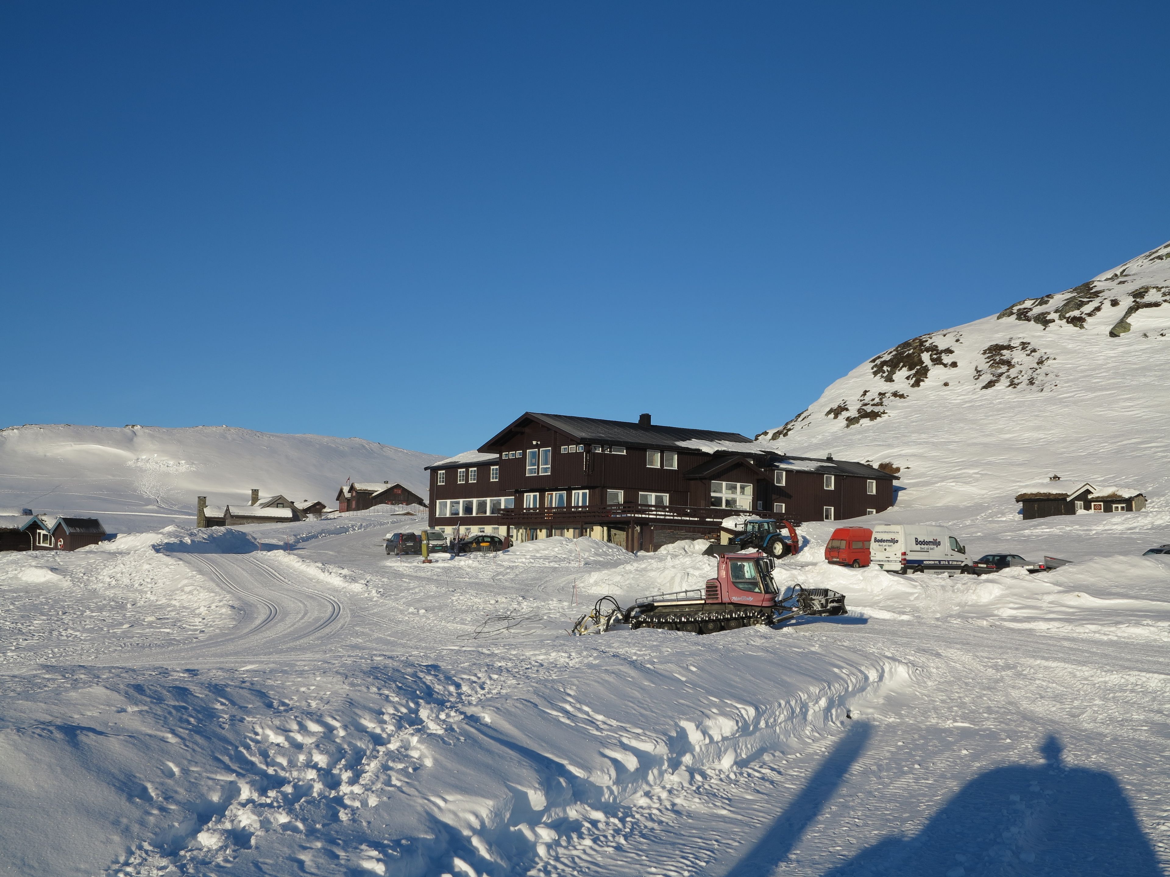 Un paisaje nevado con un edificio grande, posiblemente una cabaña, y varios vehículos.