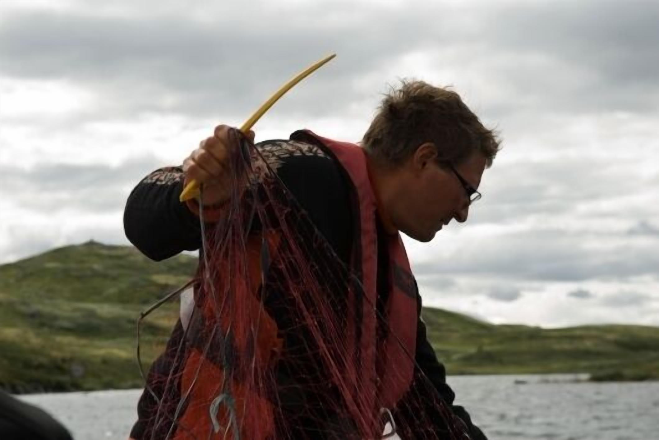 Una persona sostiene una red de pesca con un paisaje montañoso al fondo.