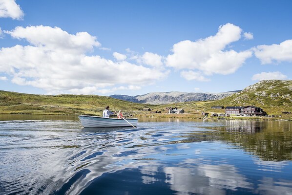 A boat on a calm lake with a mountainous backdrop and buildings in the distance.