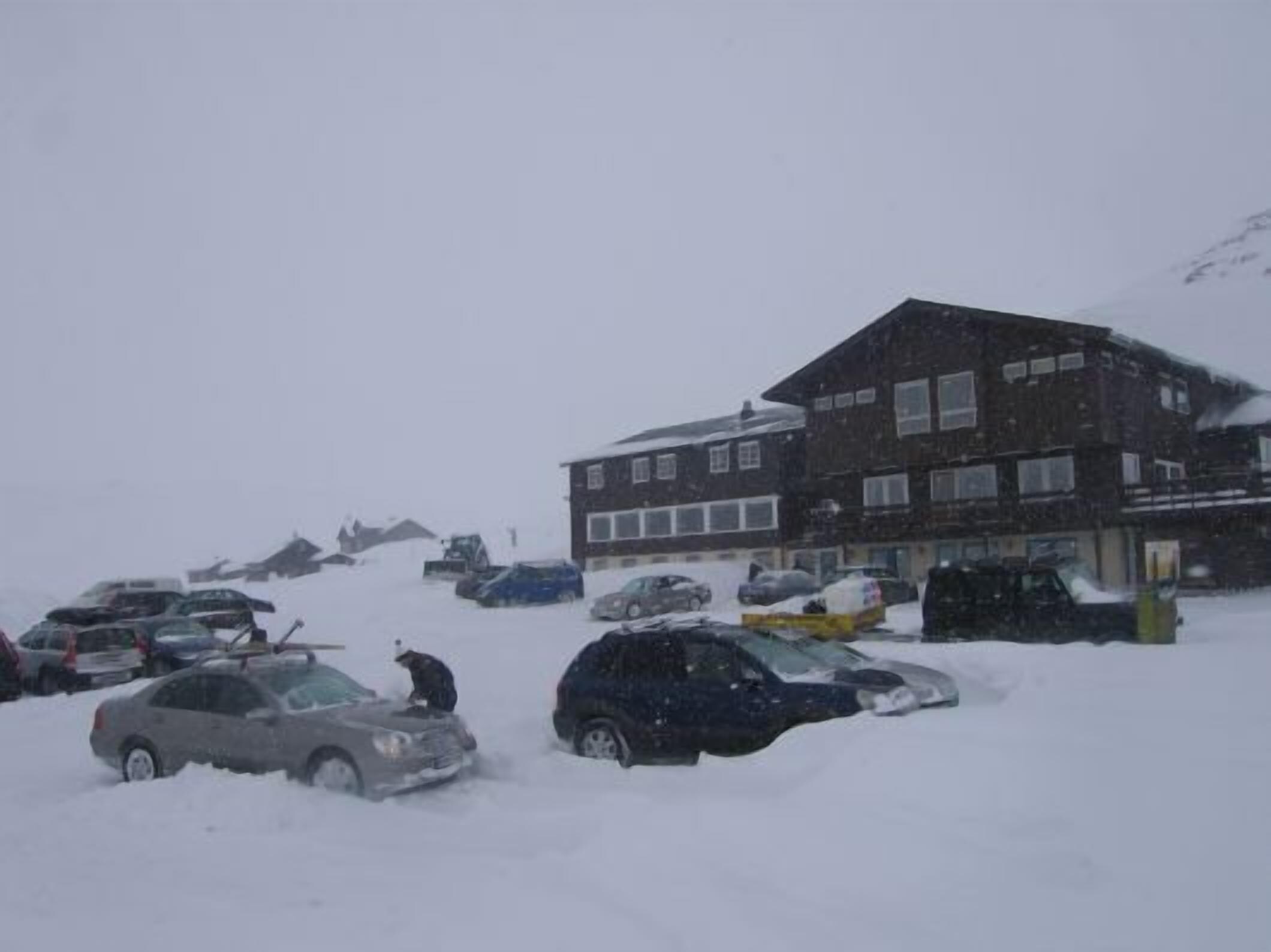 Een gebouw met meerdere ramen en een plat dak, omringd door met sneeuw bedekte geparkeerde auto's.