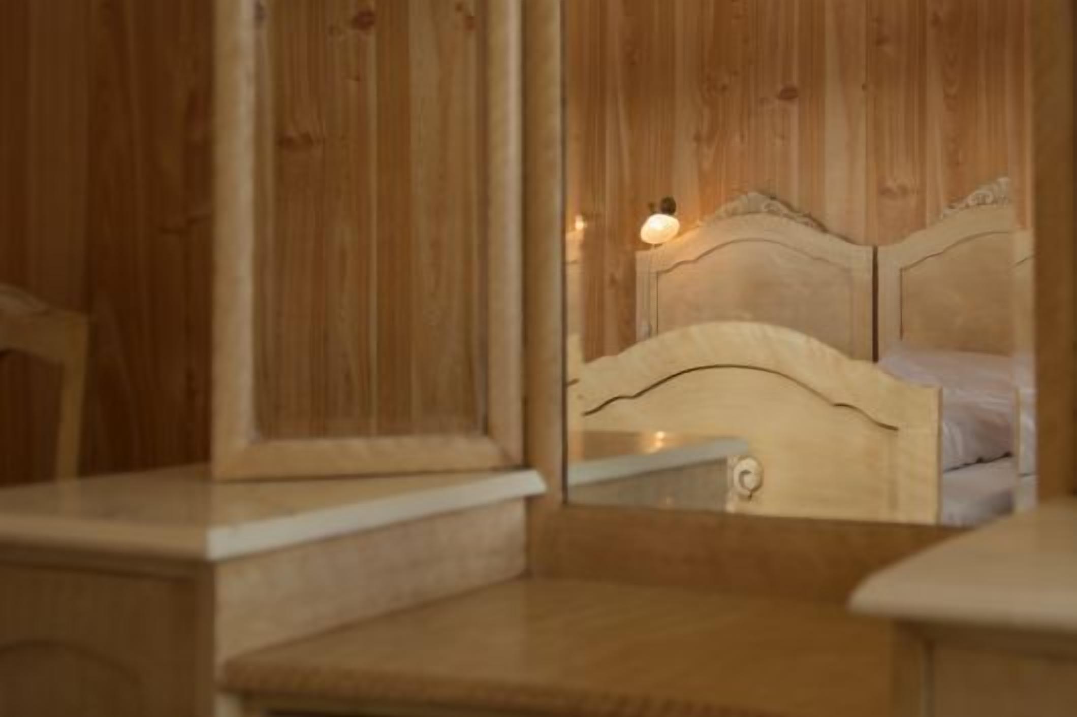 Una cama con estructura de madera, cabecera, mesita de noche y un espejo que refleja la habitación.
