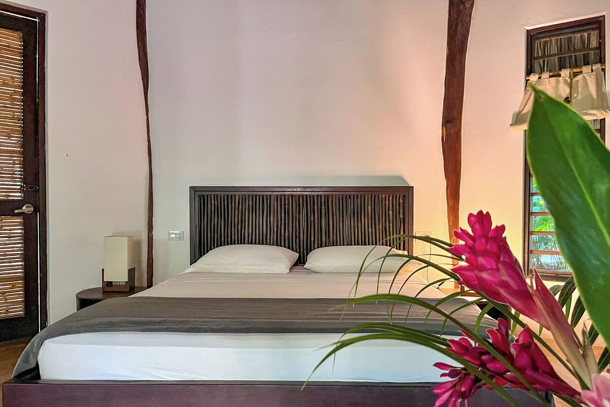 Un lit avec une tête de lit en bois, une table de chevet avec une lampe et une fenêtre avec des rideaux.