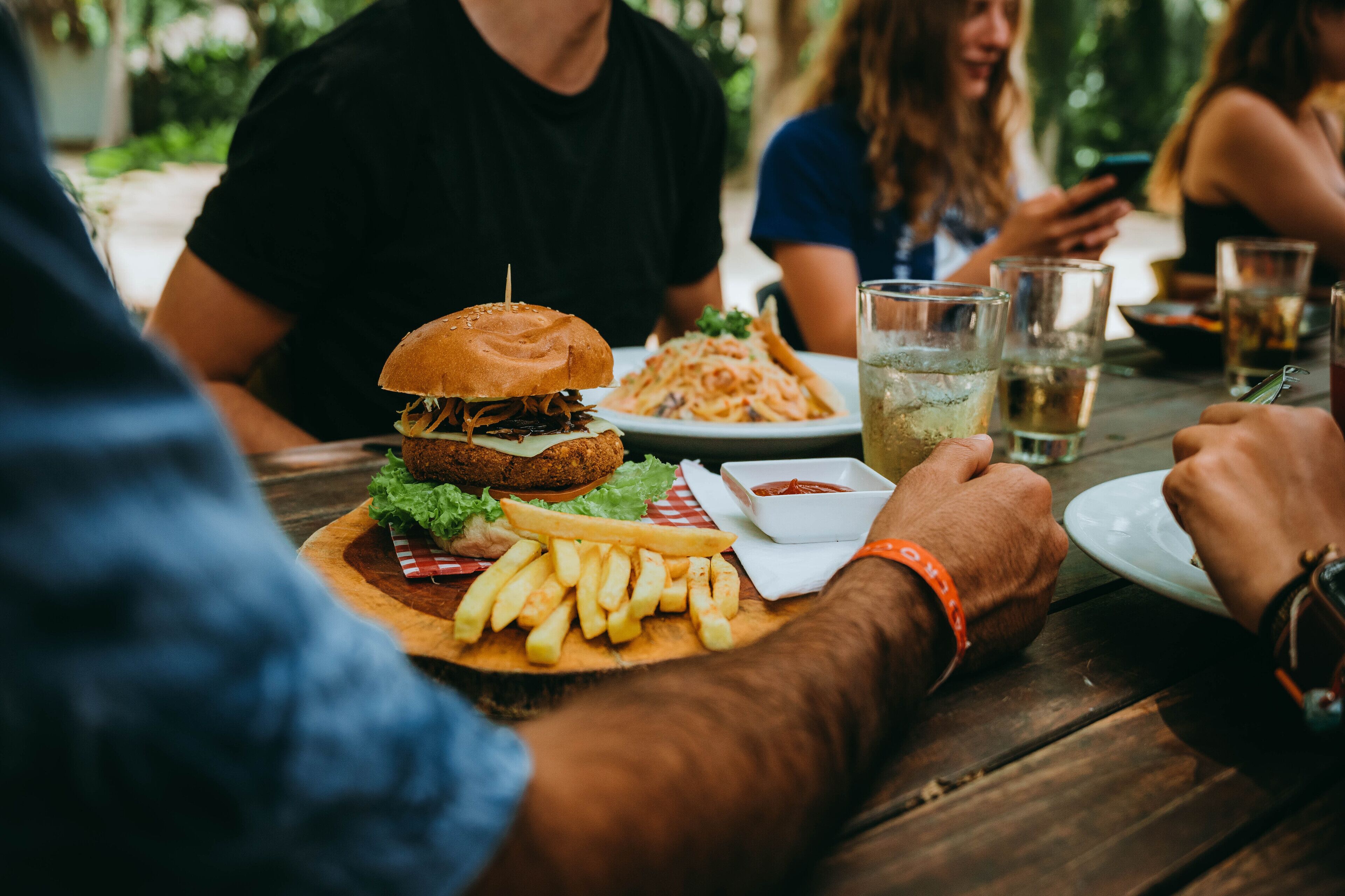 A wooden table with a burger, fries, and a drink.