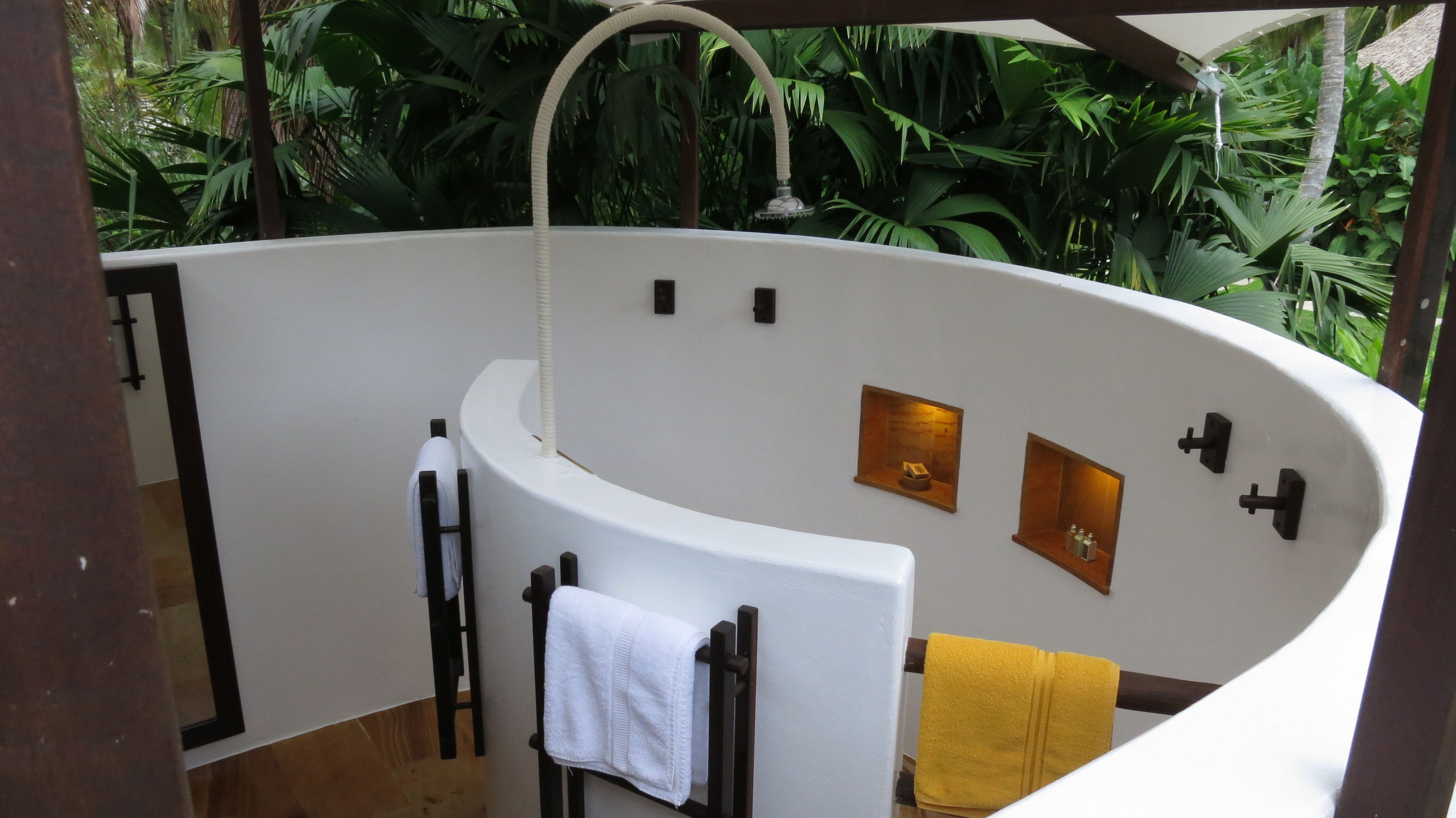 A curved shower area with a white bathtub, a towel rack with a white towel, and a yellow towel.