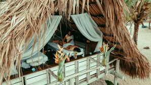 A thatched-roof hut with a bed and a small table, surrounded by plants and a wooden railing. - Viajero Tayrona Hostel & Ecohabs (Santa Marta)