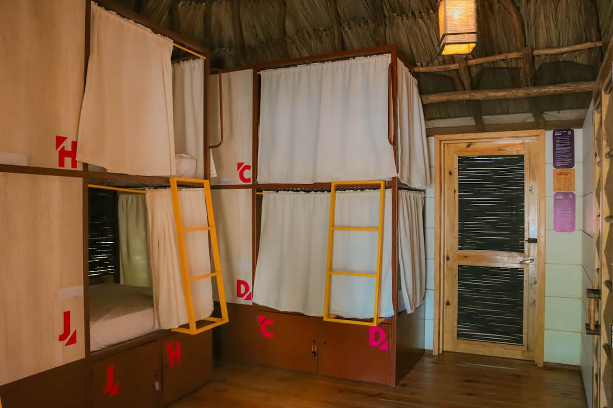 Une pièce avec des lits superposés, des murs en bois, un toit de chaume et une porte en bois dotée d’une fenêtre.