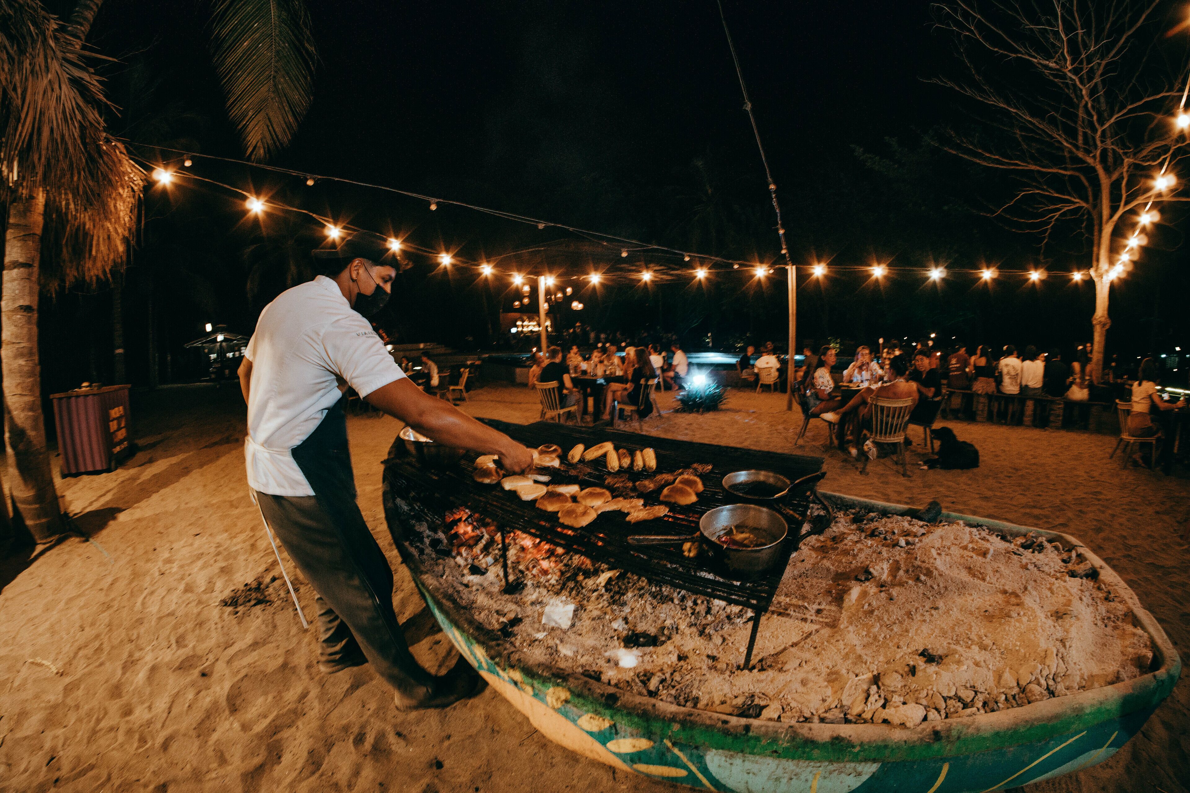 A person grilling food on a portable stove on a sandy beach at night.