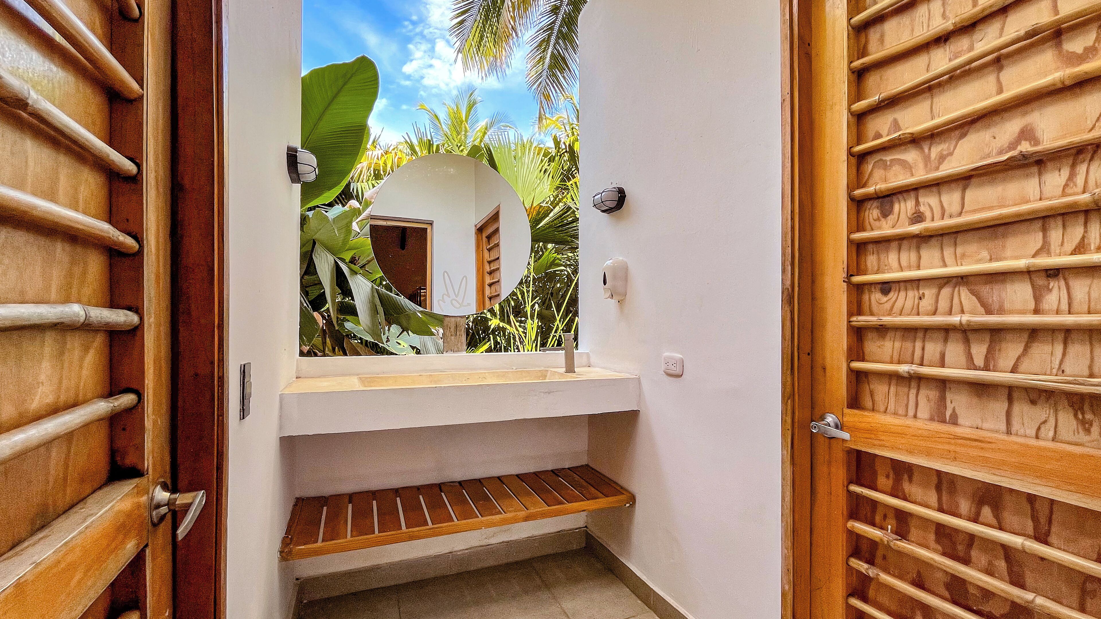 A bathroom with a wooden door, a white sink, and a small wooden shelf.