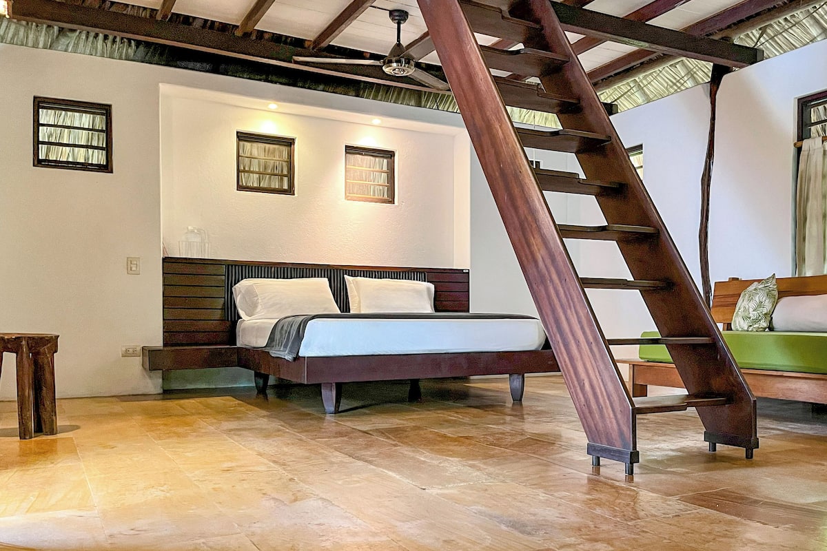Une chambre à coucher avec un lit, une échelle en bois, un canapé vert et une fenêtre avec des rideaux.