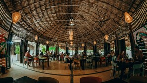 An open-plan restaurant with a thatched roof, multiple seating areas, and hanging pendant lights. - Viajero Tayrona Hostel & Ecohabs (Santa Marta)