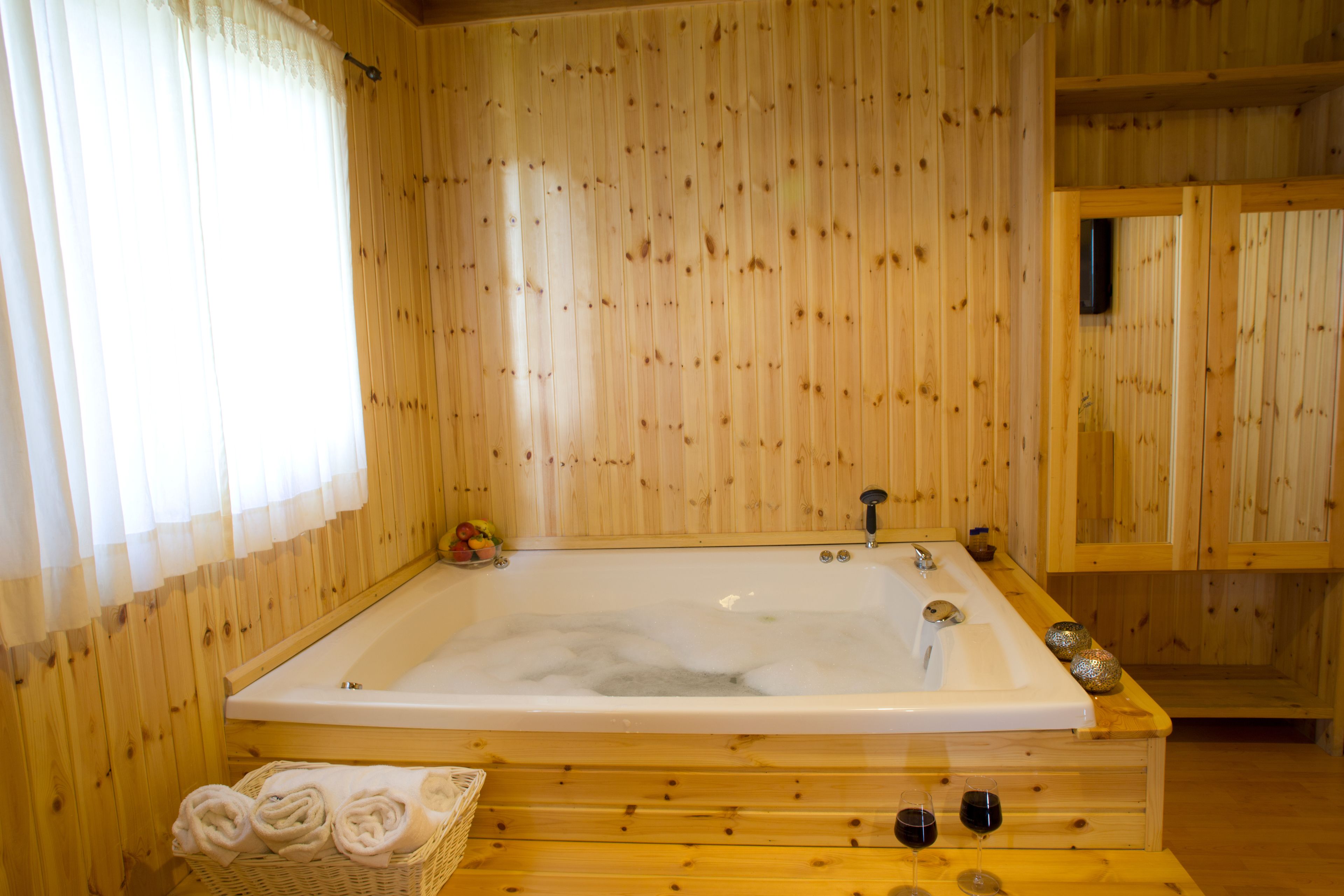 A wooden cabin with a large bathtub, a wicker basket with towels, and a wooden shelf with decorative items.