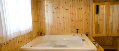 A wooden cabin with a large bathtub, a wicker basket with towels, and a wooden shelf with decorative items.