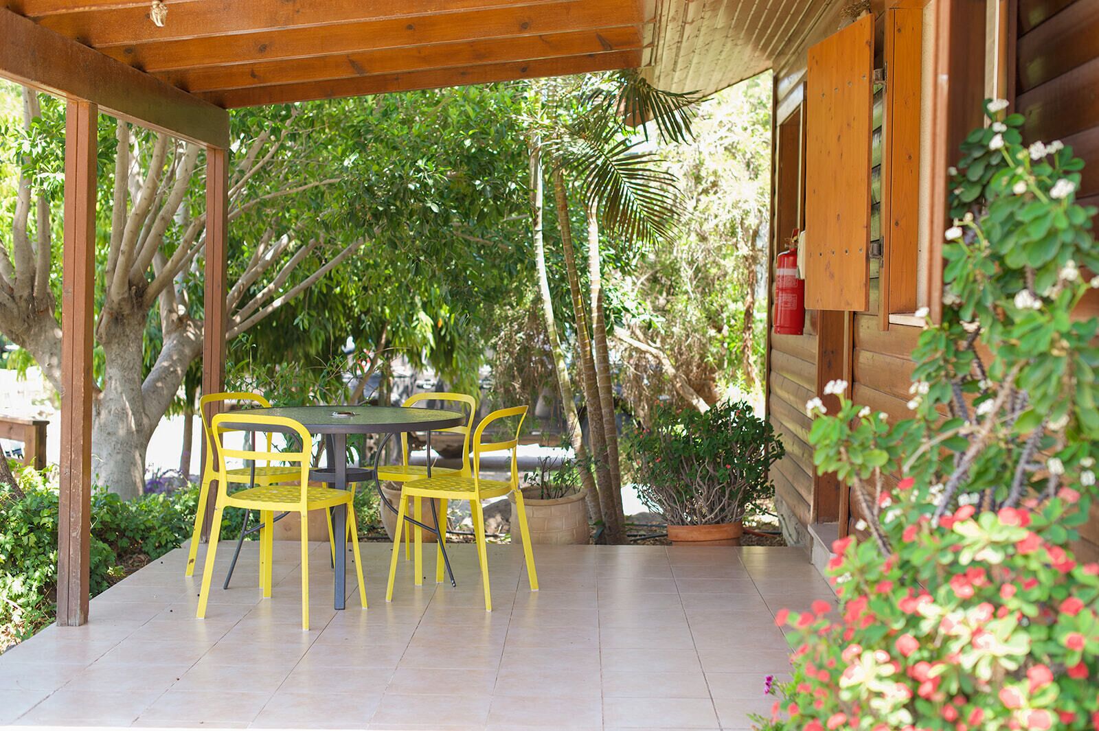 An outdoor patio with a wooden pergola, a round table, and yellow chairs.
