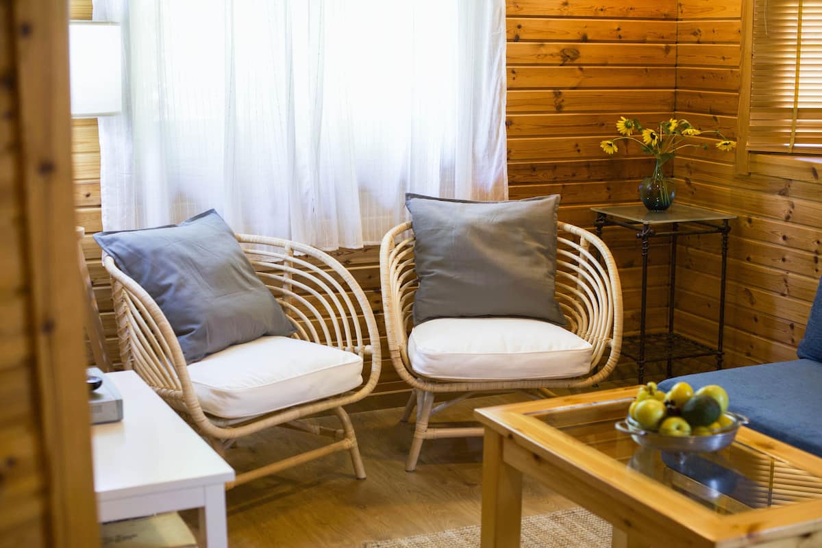 A cozy room with wicker chairs, a small table with a bowl of fruit, and a vase with flowers.