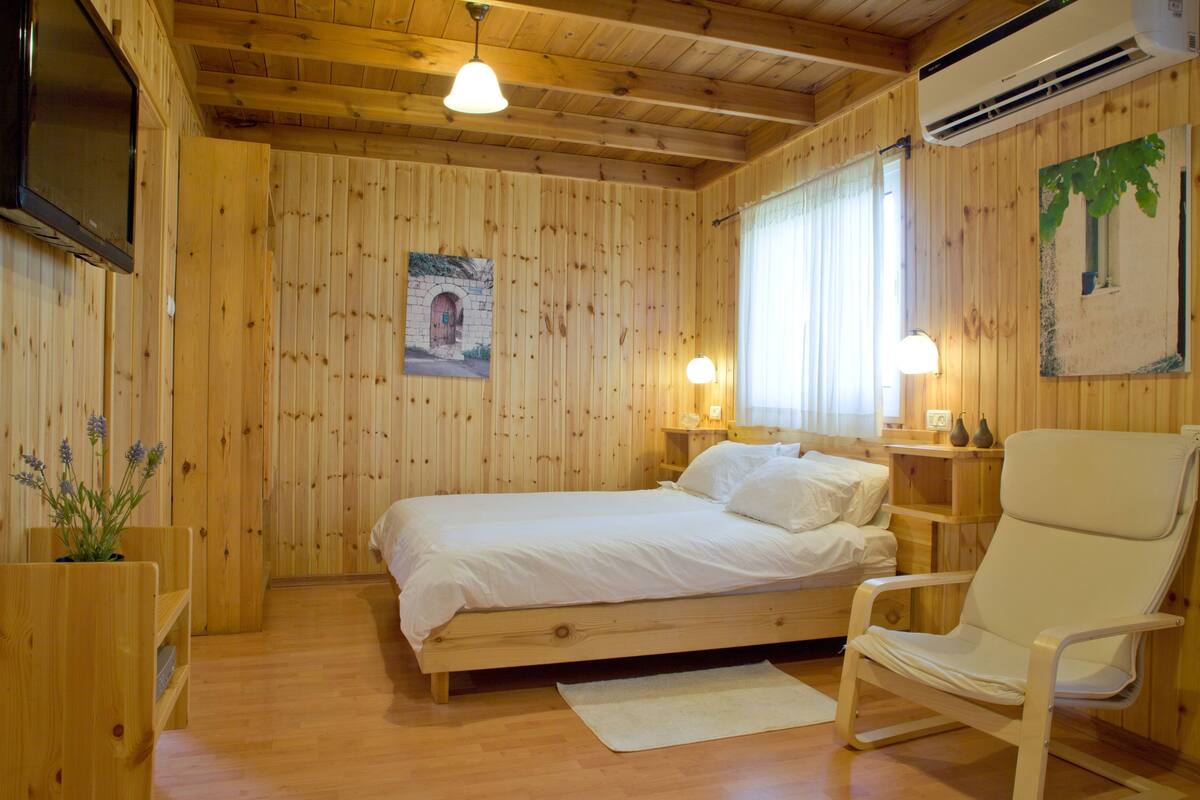 A wooden-paneled room with a bed, a chair, a TV, and a painting on the wall.