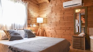 A wooden-paneled room with a bed, a lamp, and an air conditioning unit. - Naomi's B&B (Ramot)