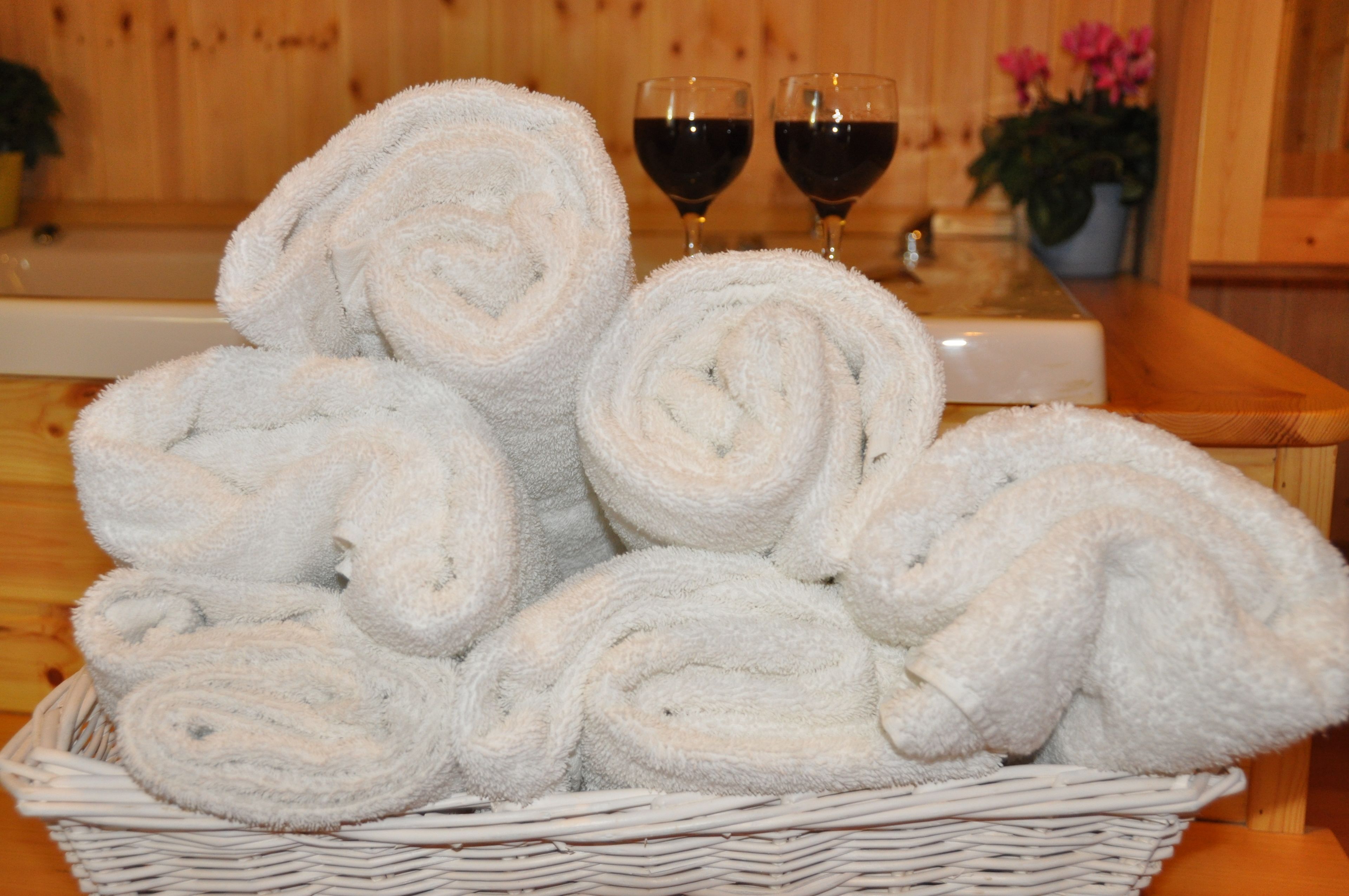 A basket of white towels and two glasses of red wine on a wooden table.