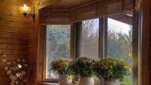 A wooden cabin interior with a window sill holding three white vases with yellow flowers. - Naomi's B&B (Ramot)