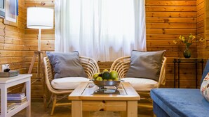 A cozy cabin interior with a wooden floor, a sofa with cushions, a small table with a fruit bowl, and a lamp. - Naomi's B&B (Ramot)