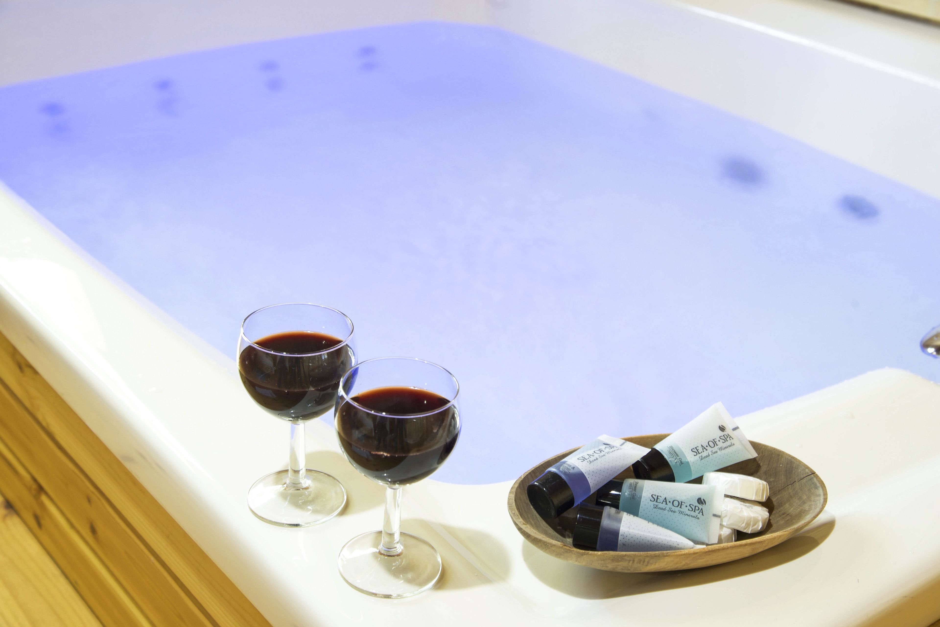 A bathtub with two glasses of red wine and a wooden bowl containing bottles and tubes.