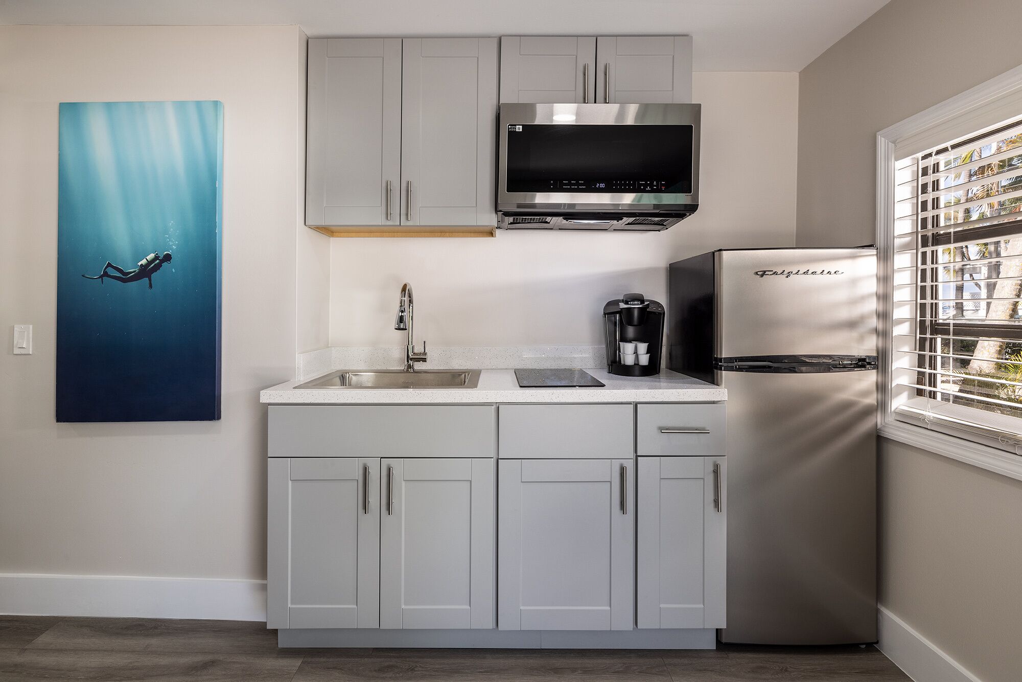 A modern kitchen with grey cabinets, a stainless steel refrigerator, a coffee maker, and a digital microwave.