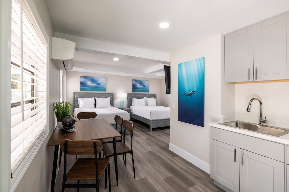 Une chambre d’hôtel moderne comprenant un coin repas, deux lits, une cuisine et des œuvres d’art accrochées aux murs.