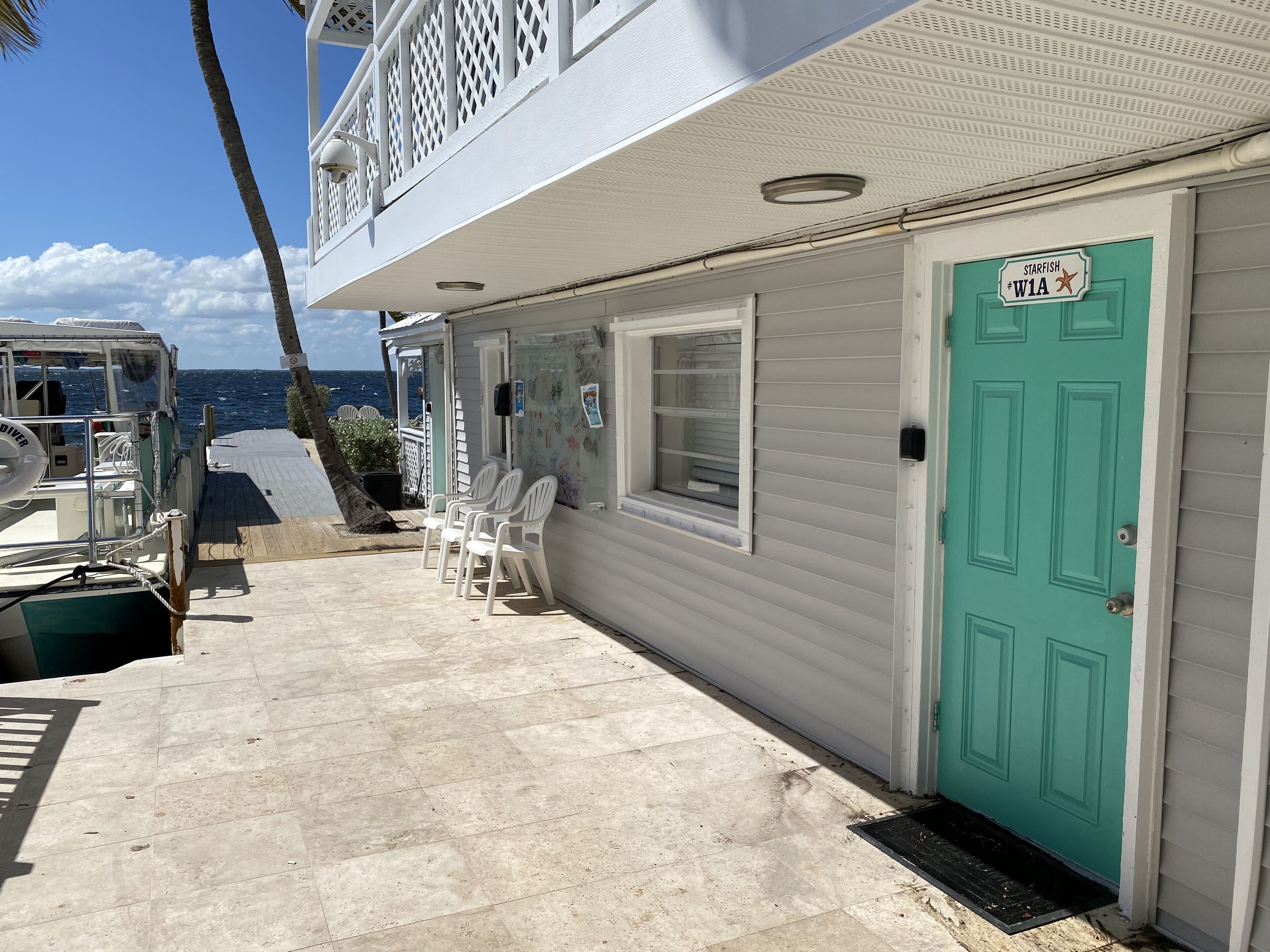 A building with a green door, white exterior walls, and a balcony with white chairs.