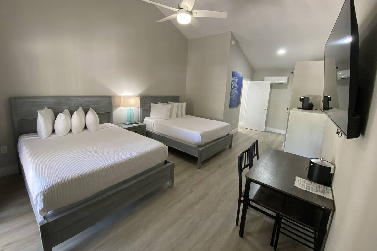 Une chambre d’hôtel avec deux lits, un bureau, une chaise, un ventilateur de plafond et un téléviseur à écran plat.