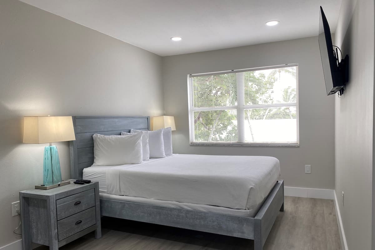 Une chambre à coucher avec un lit, des tables de chevet, une lampe, un téléviseur et une fenêtre avec des stores.