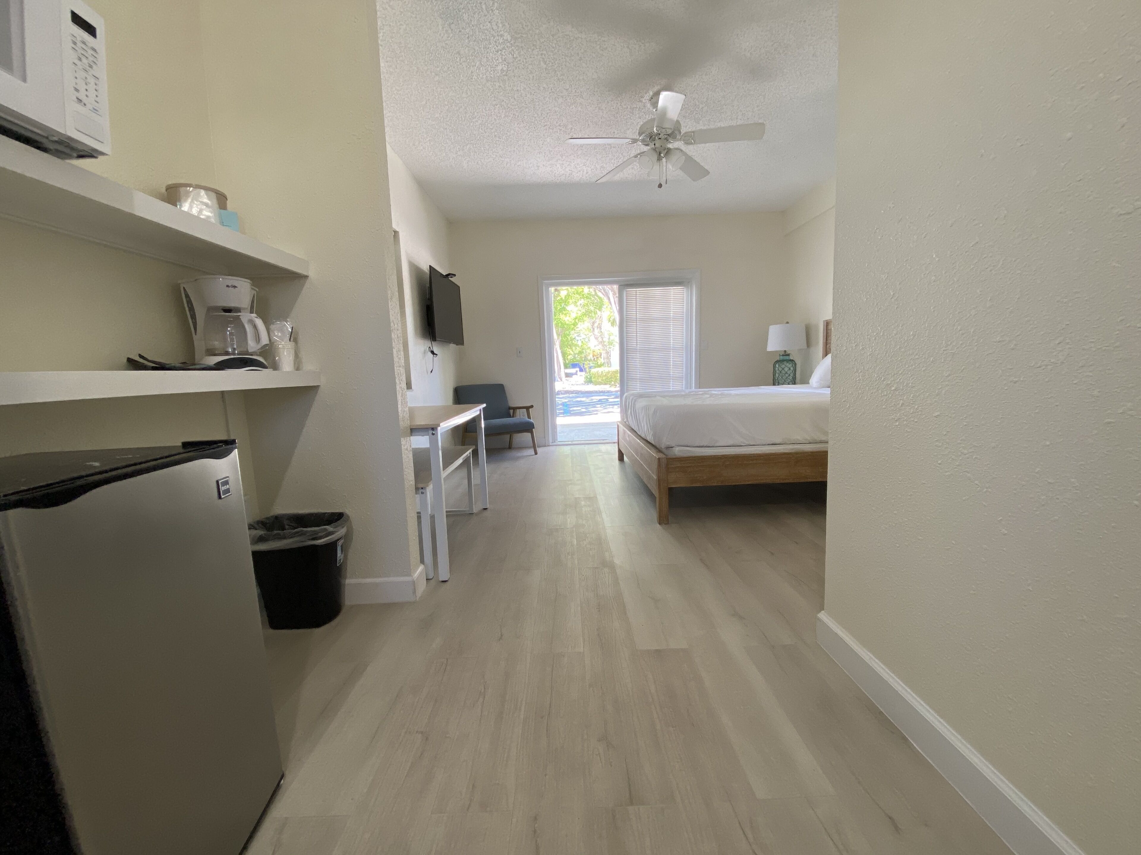 A compact hotel room with a kitchenette, a bed, a television, and a ceiling fan.