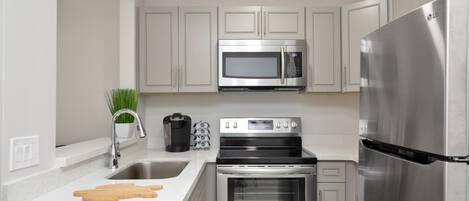 A modern kitchen with stainless steel appliances, a sink, and a countertop with a cutting board.