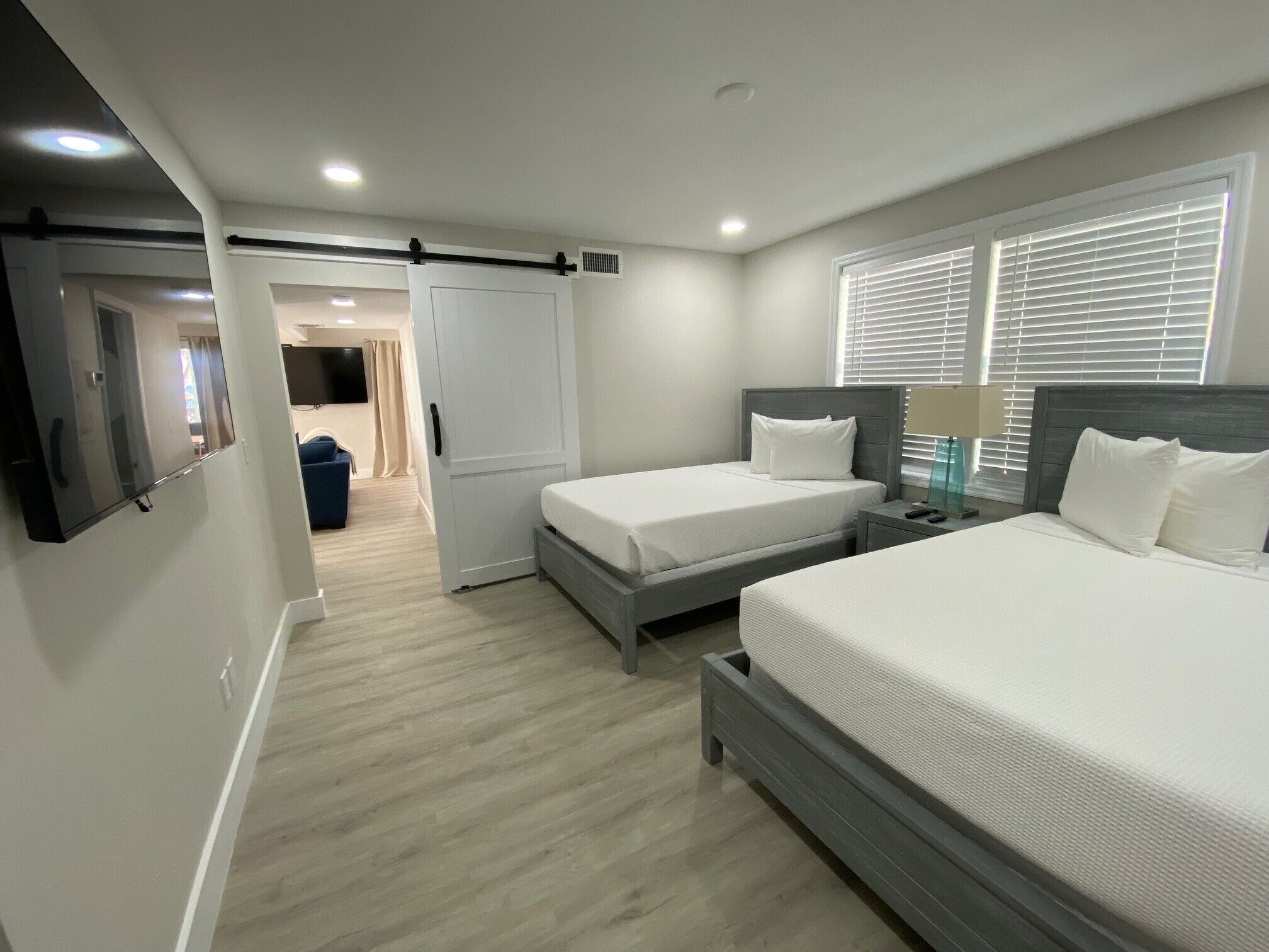 Una habitación de hotel moderna con dos camas individuales, una cama grande, un televisor, un escritorio y una ventana con persianas.
