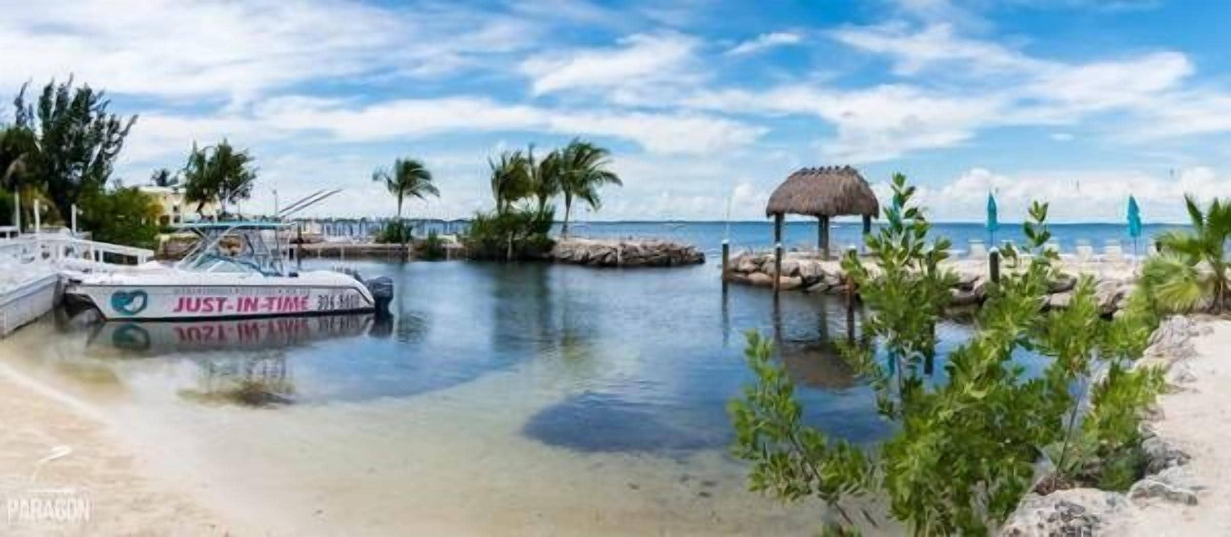 Un bote amarrado en una playa con una estructura de techo de paja y palmeras al fondo.
