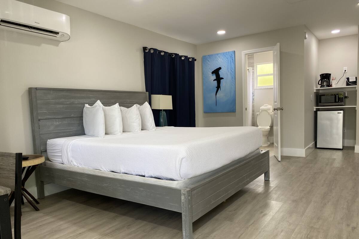 Un lit bien fait, avec des draps blancs, une tête de lit en bois et un rideau bleu foncé.